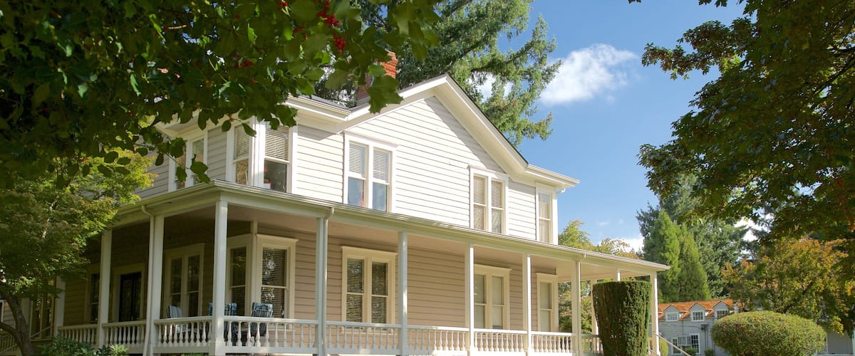A two-story house with a porch, surrounded by well-maintained lawns and trees.