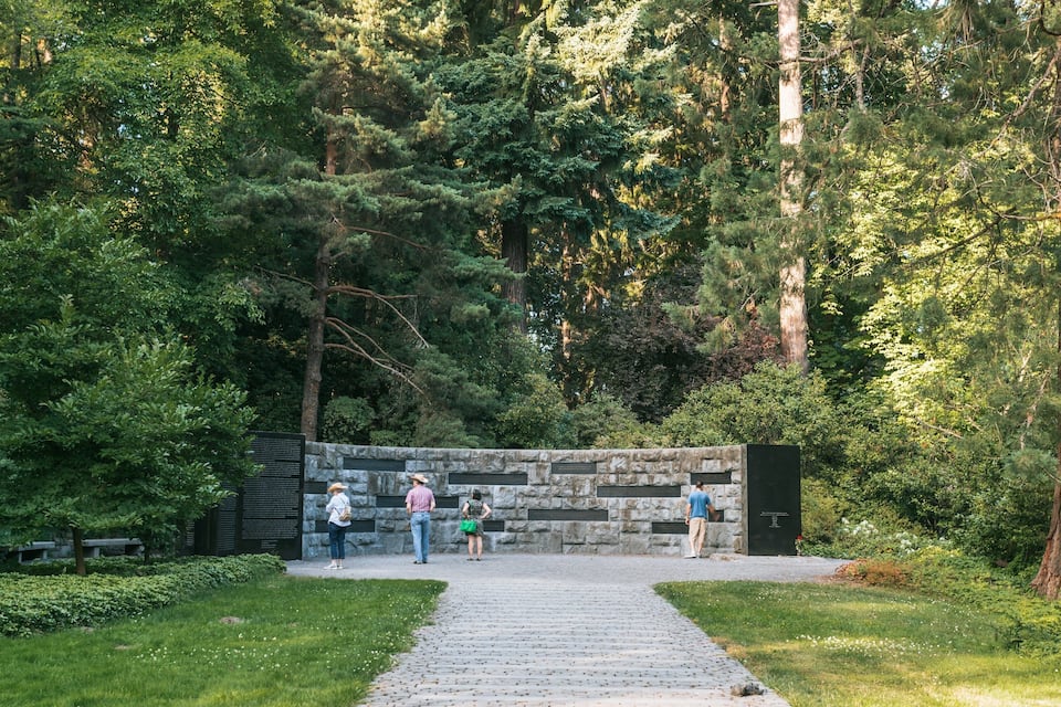 A stone wall with inscriptions, surrounded by dense forest and a cobblestone path.