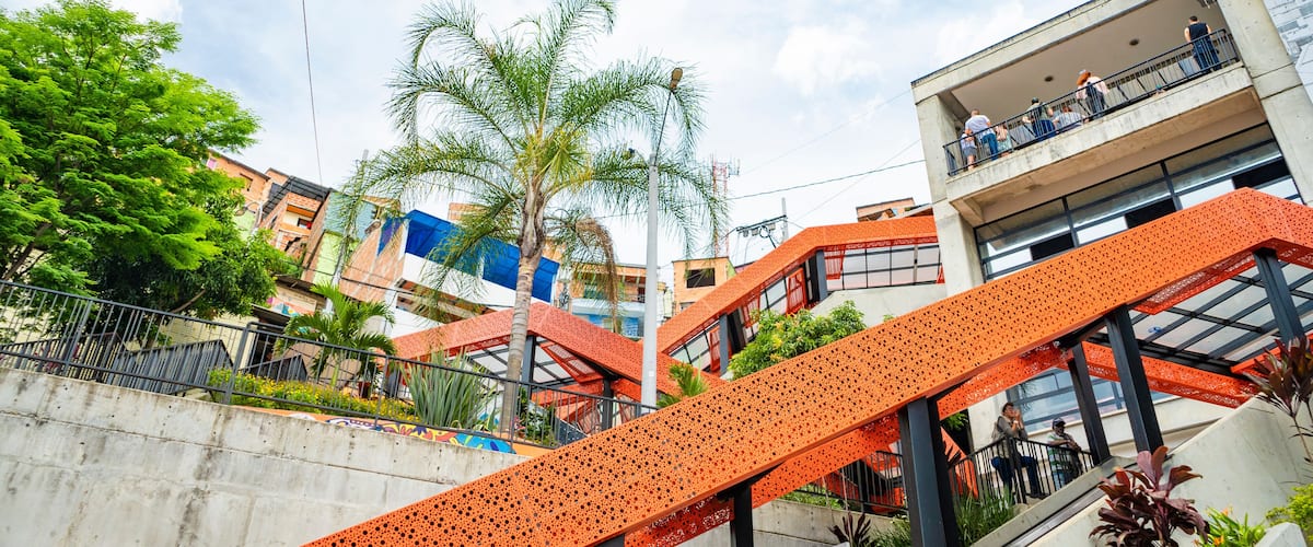 A multi-level outdoor staircase with orange railings, surrounded by buildings and palm trees.