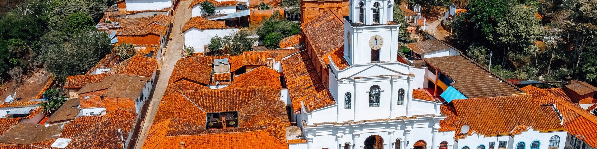 A white church with a bell tower surrounded by red-tiled buildings in a hilly town.