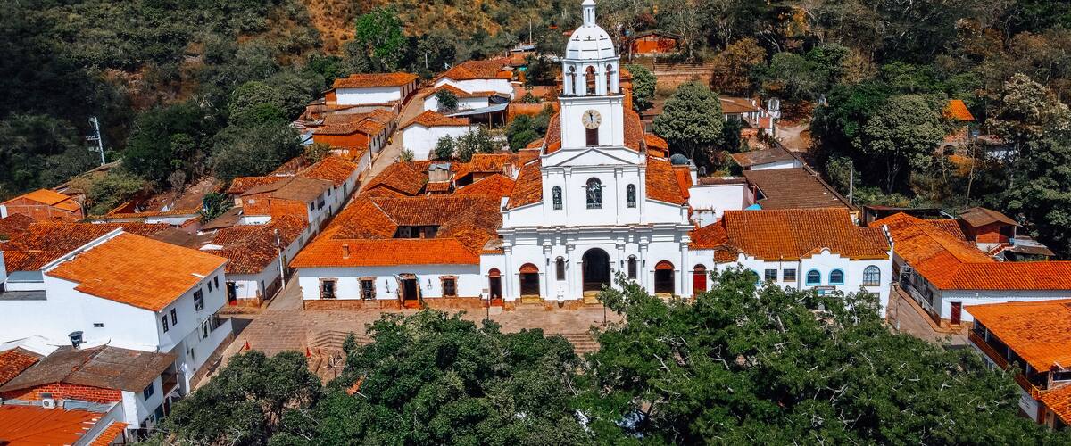 A white church with a bell tower surrounded by red-tiled buildings in a hilly area.