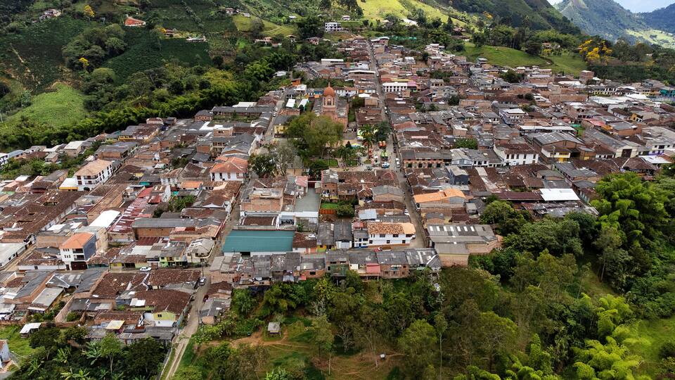 An aerial view of a densely packed town with a prominent church, surrounded by lush greenery and hills.