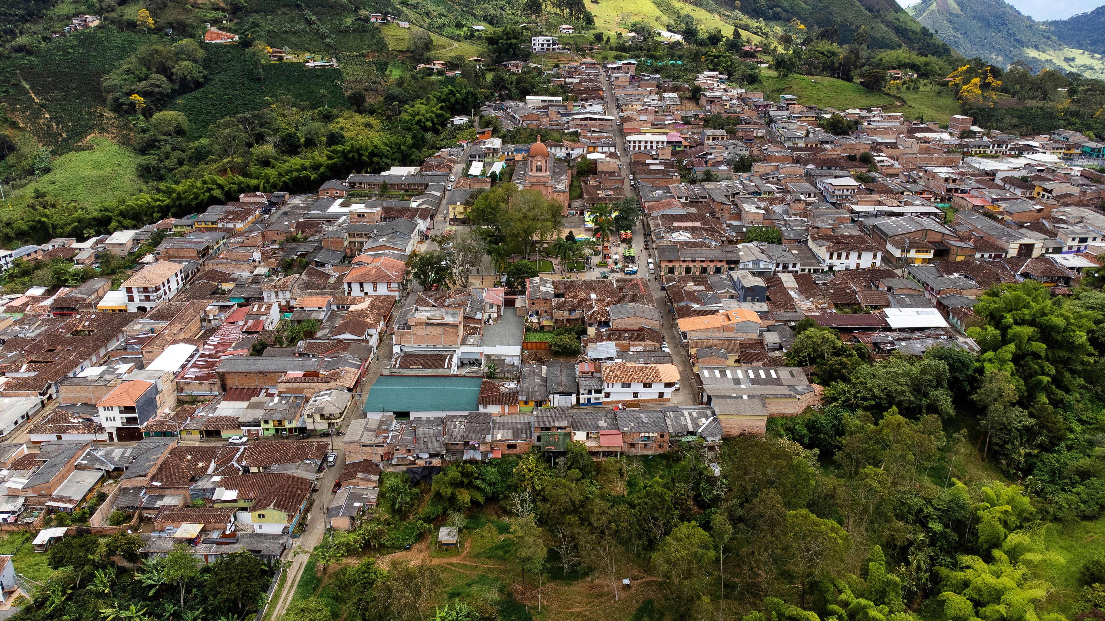 An aerial view of a densely packed town with a prominent church, surrounded by lush greenery and hills.