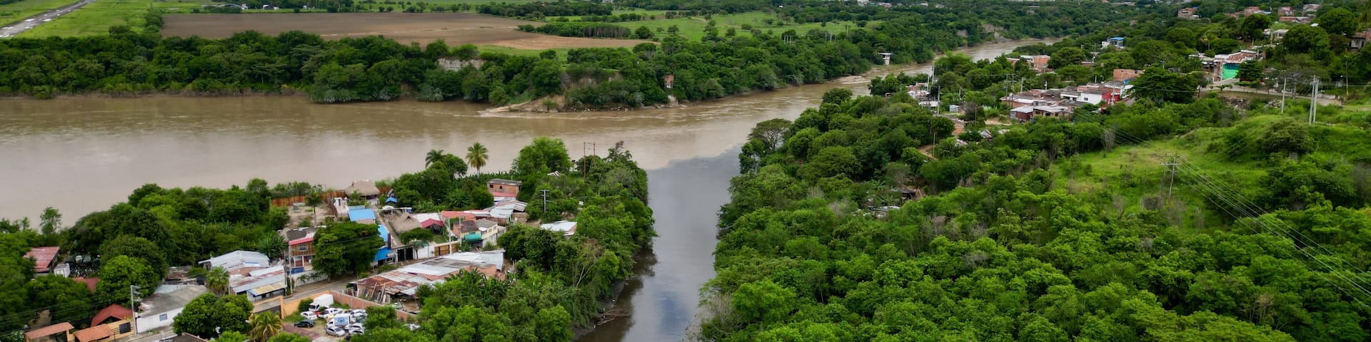 A river winding through a densely forested area with a small settlement on the riverbank.