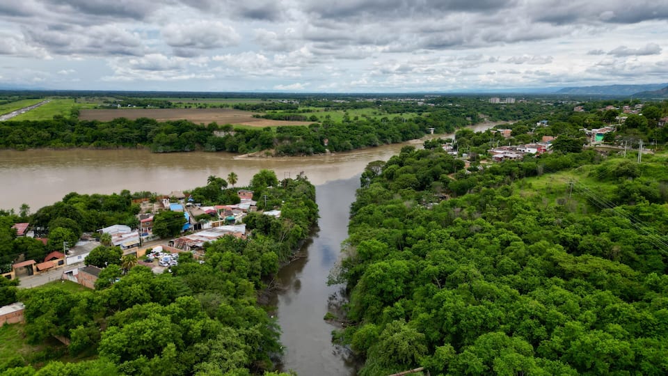 A river winding through a densely forested area with a small settlement on the riverbank.