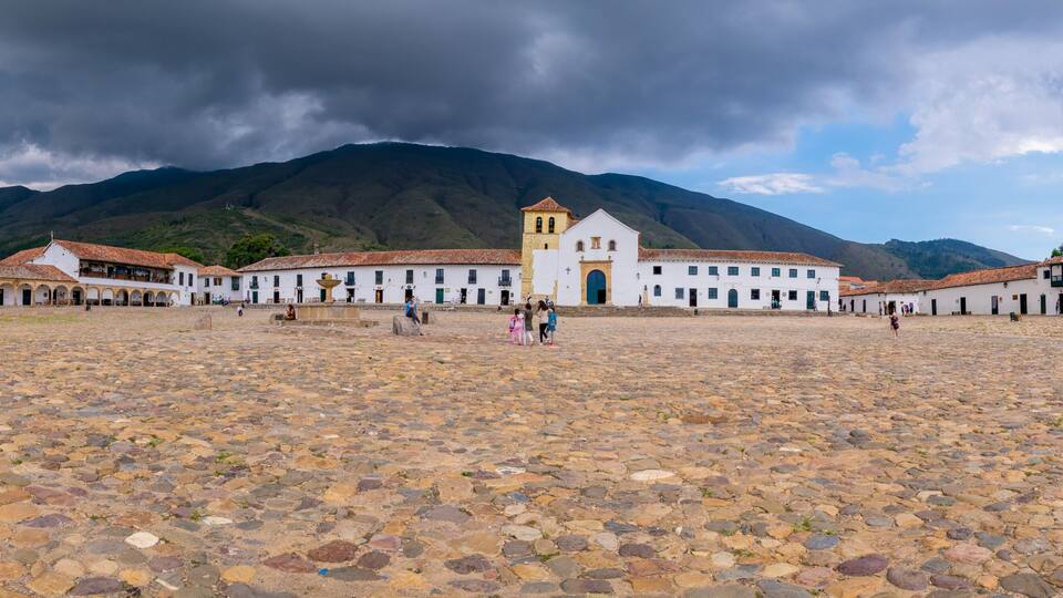A cobblestone plaza with white buildings and a church with a bell tower.