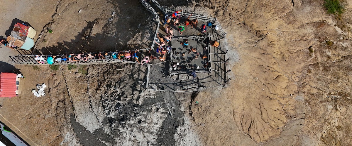 An aerial view of a makeshift bridge over a deep ravine with people crossing.