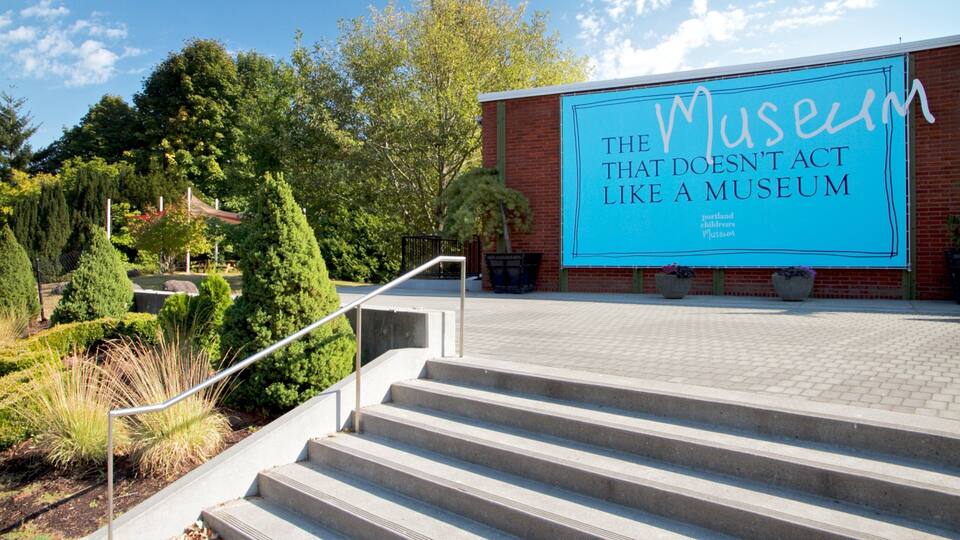 A museum entrance with a large sign, steps, and surrounding greenery.