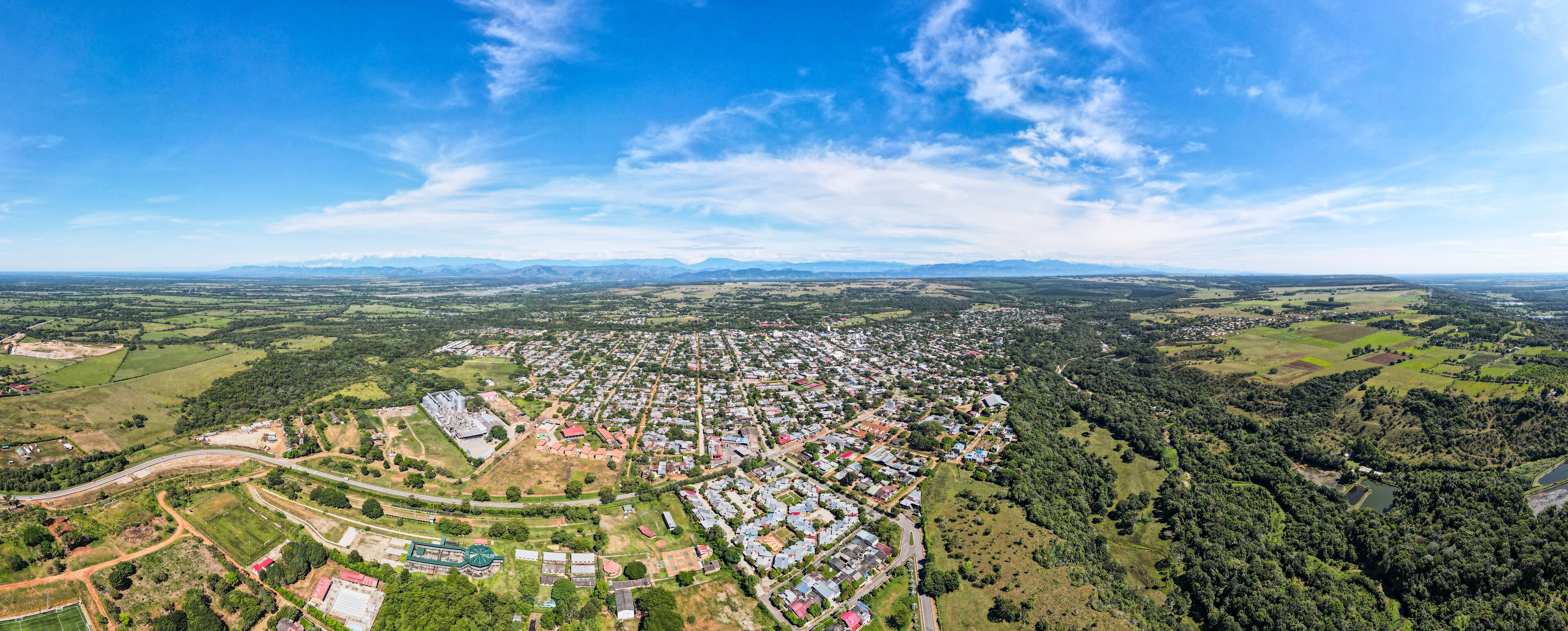 An aerial view of a town with a mix of residential areas, green fields, and a large building complex.