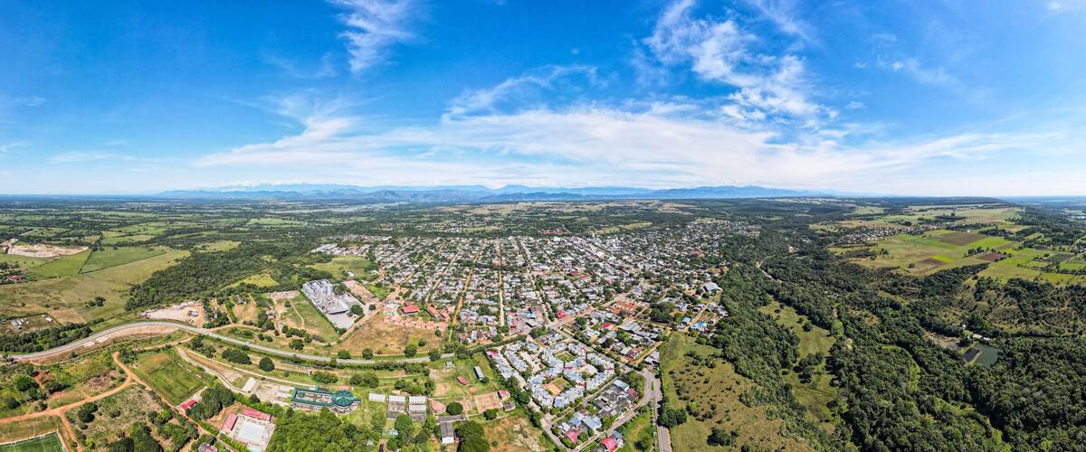 An aerial view of a town with a mix of residential areas, green fields, and a large building complex.