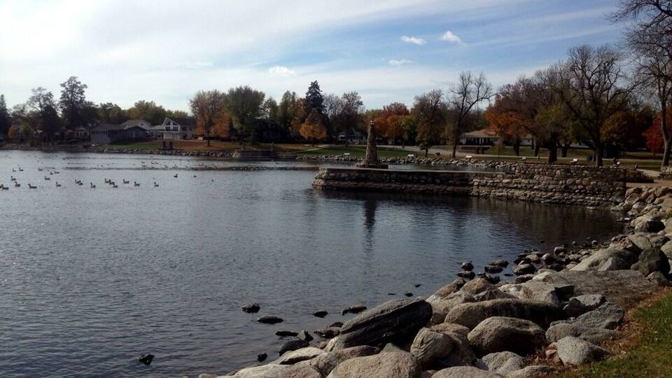 A lake with ducks, a stone wall, and autumn-colored trees.