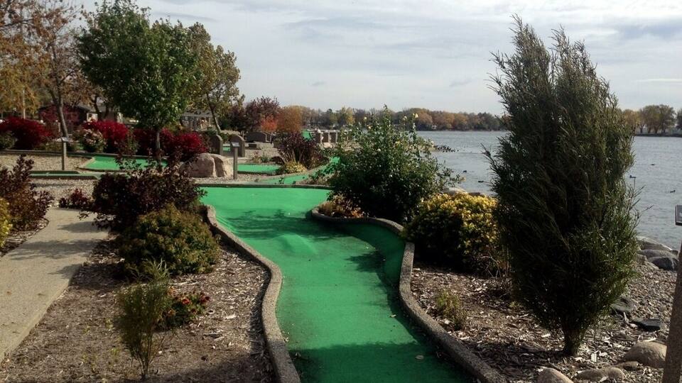 A miniature golf course with a green putting green, surrounded by landscaped areas and trees.