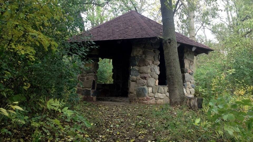 A stone gazebo with a red roof surrounded by trees and foliage.