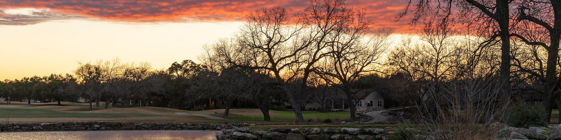 Dramatic sunset lighting a layer of clouds and reflected in the still water of Legacy Hills Park near Georgetown, Texas