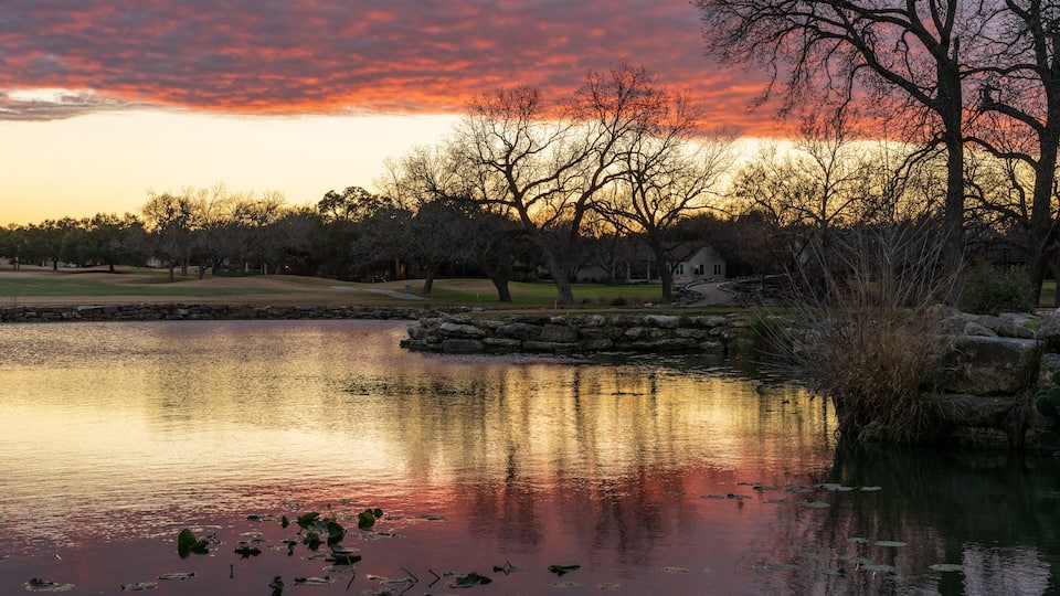 A sunset over a calm lake with reflections of trees and a stone bridge.