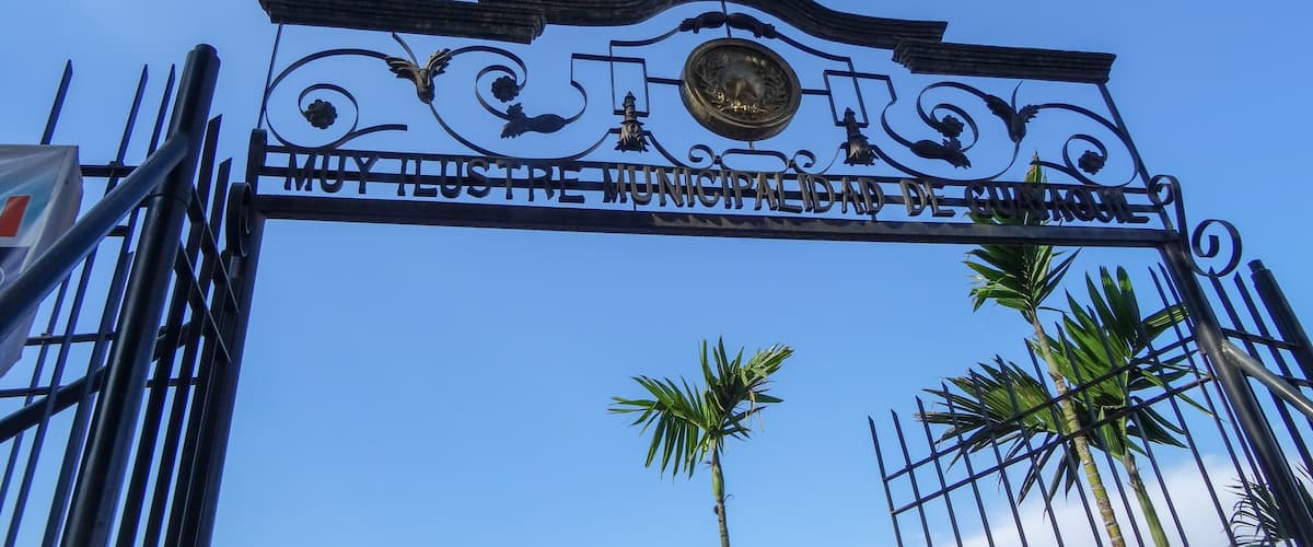 A metal gate with ornate designs and the inscription "MUY ILUSTRE MUNICIPALIDAD DE GUAMOTE".