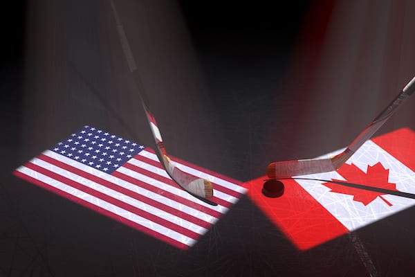 Hockey puck, hockey sticks and the image of the Unites States and Canadian flag on the ice.
