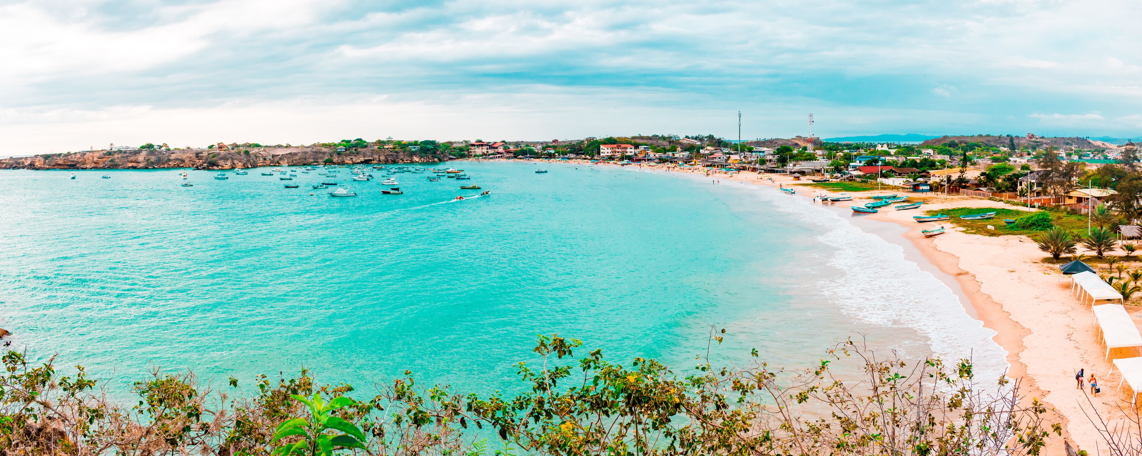 A coastal town with turquoise waters, a sandy beach, and boats.