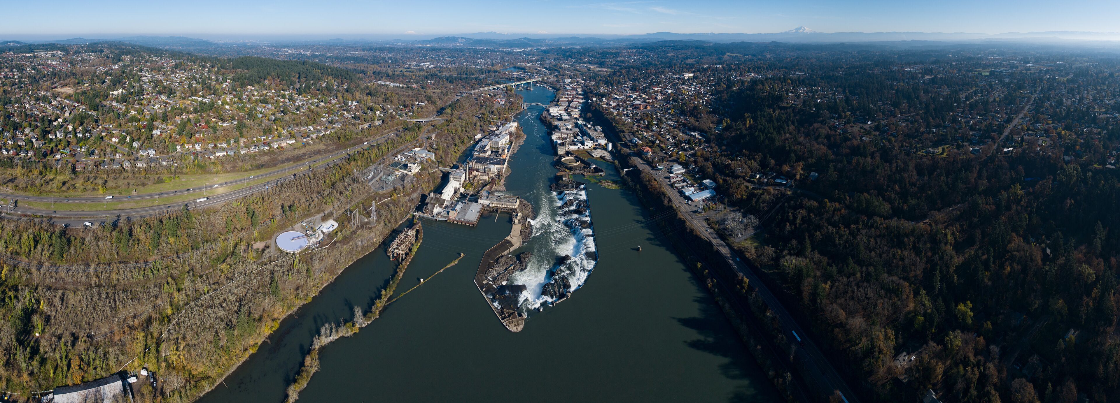 An aerial view of a river with a bridge, surrounded by dense forests and urban areas.