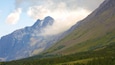 Une chaîne de montagnes avec une vallée boisée et des nuages au sommet.