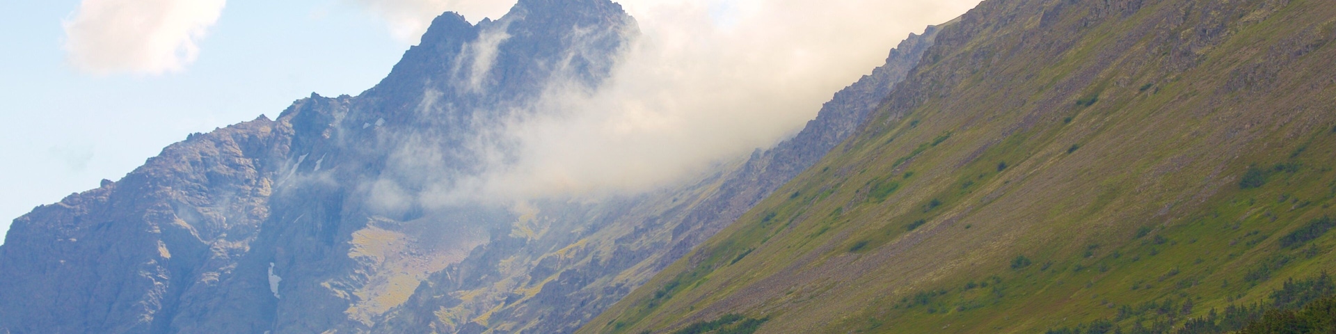 Una cordillera con un valle boscoso y nubes en la cima.