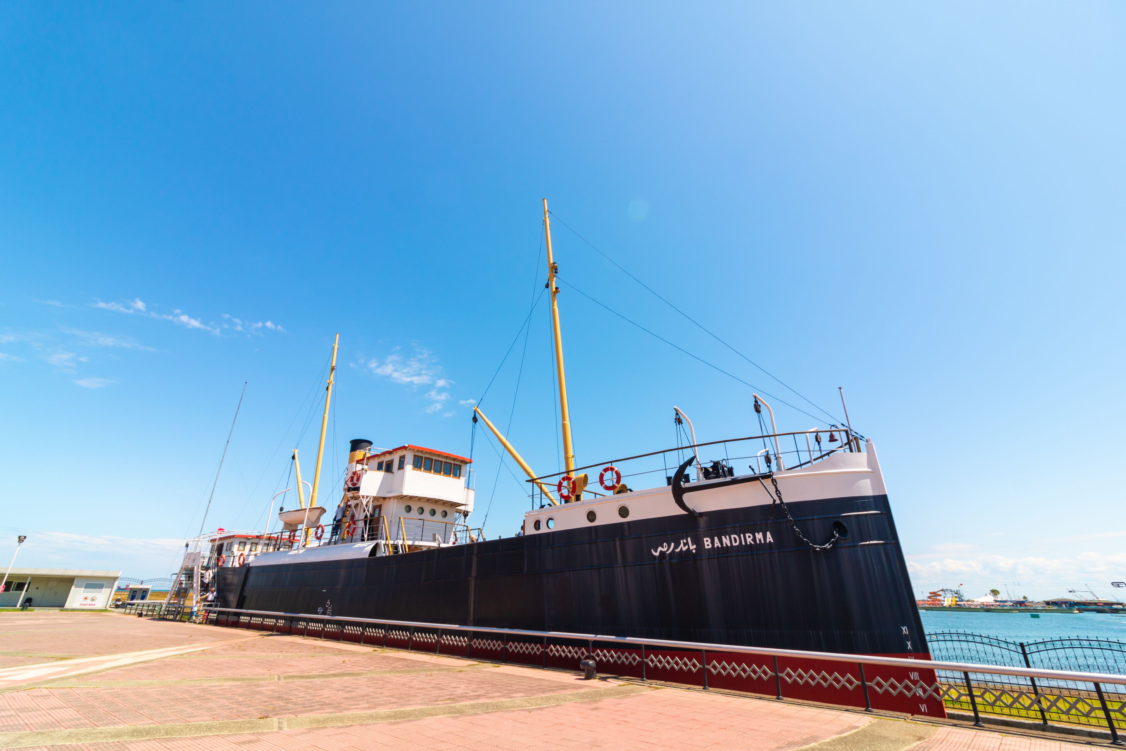 Un gran barco llamado 'Bandirma' atracado en un puerto bajo un cielo azul despejado.