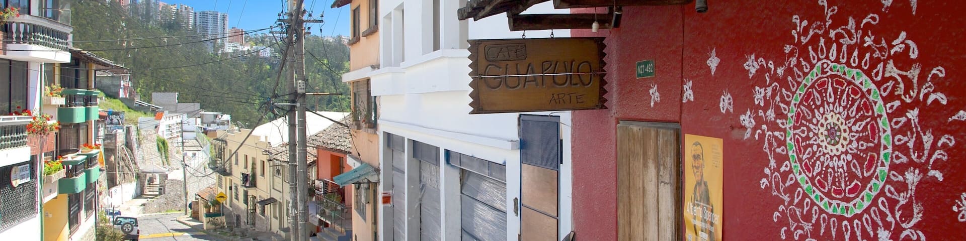 A narrow street with buildings, a sign for 'Cafe Guapo Arte', and a mural on a red wall.