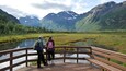 Eine Holzbrücke über einem stillen See, im Hintergrund Berge.