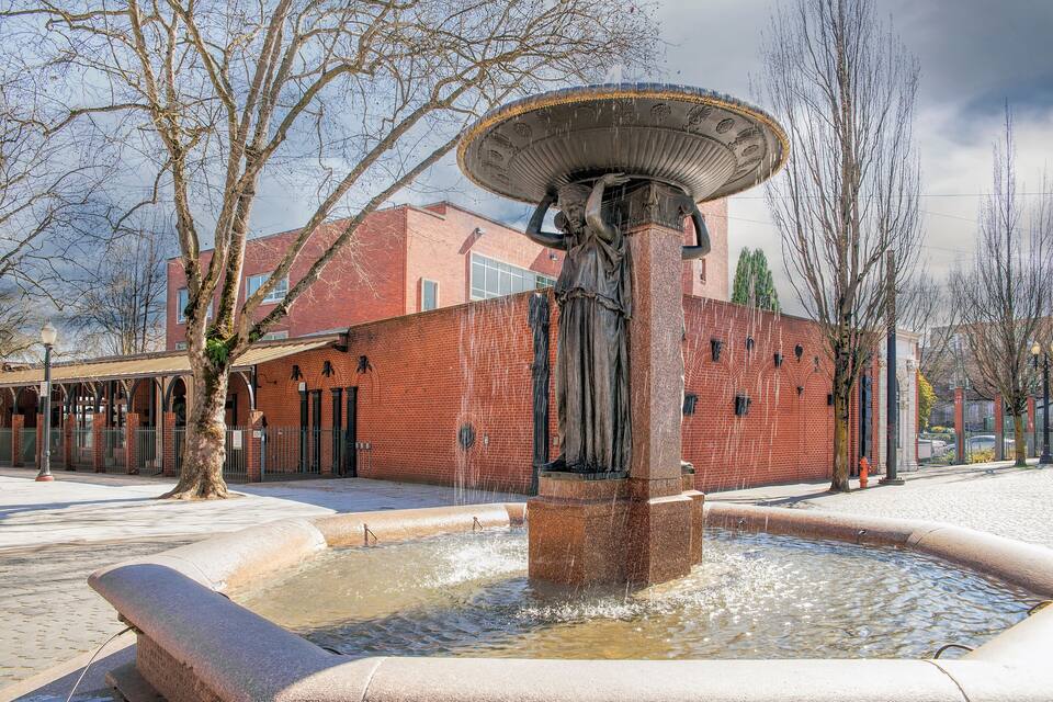 A fountain with a statue, surrounded by a brick building and bare trees.