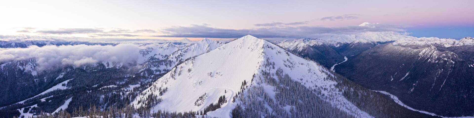 A snow-covered mountain peak with a forested valley below.