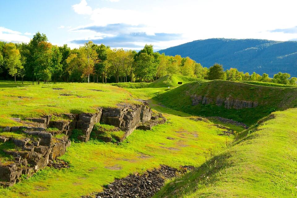 Un campo cubierto de hierba con antiguas ruinas de piedra y una colina al fondo.