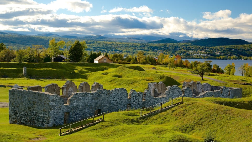A stone ruin with a staircase, surrounded by lush green hills and a lake in the background.