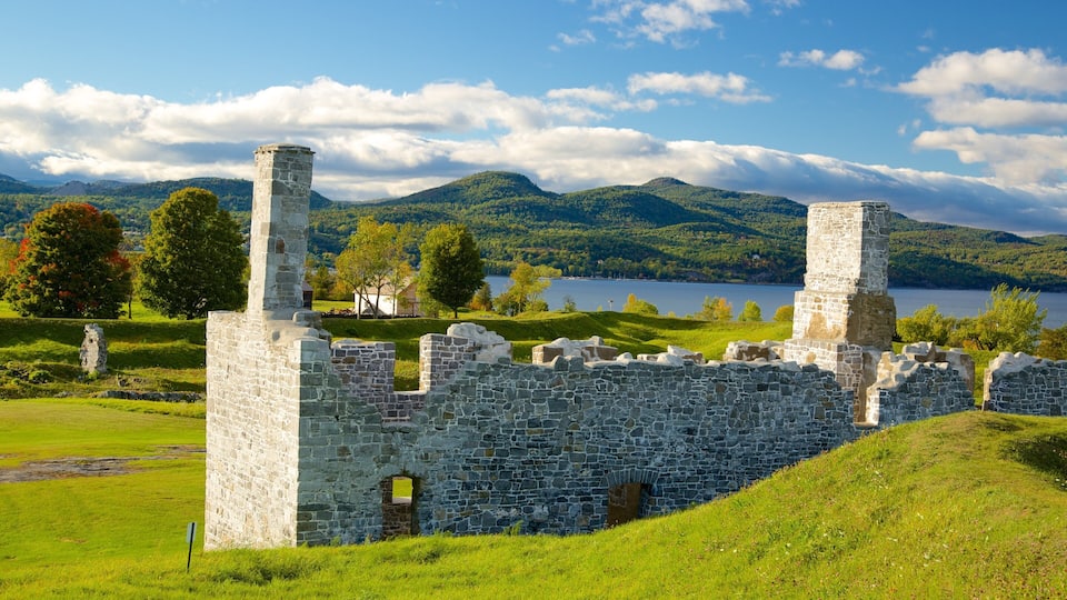 A historic stone ruin with a lake and mountains in the background.