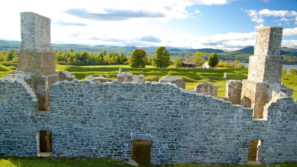 A stone castle ruin with battlements, set against a backdrop of rolling hills and a lake.