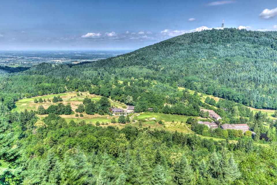 A lush green landscape with a golf course, residential buildings, and a tower on a hill.