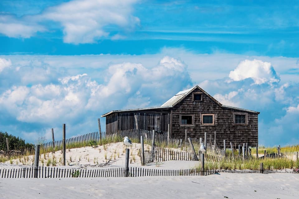 A wooden cabin on a sandy hill with a wooden fence in the foreground.