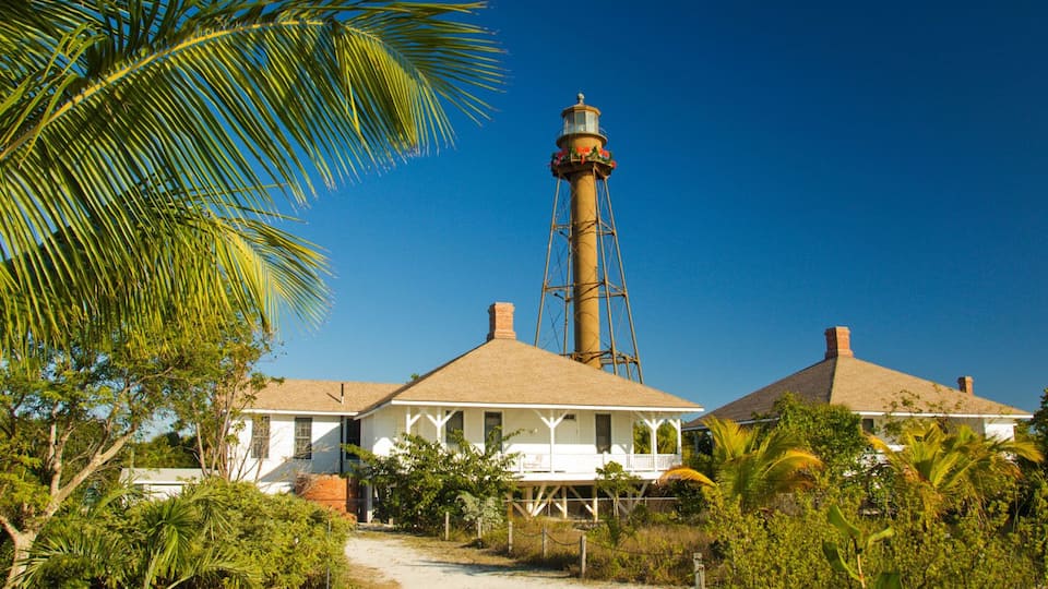 A lighthouse with a tall tower and a white building with a porch in front.