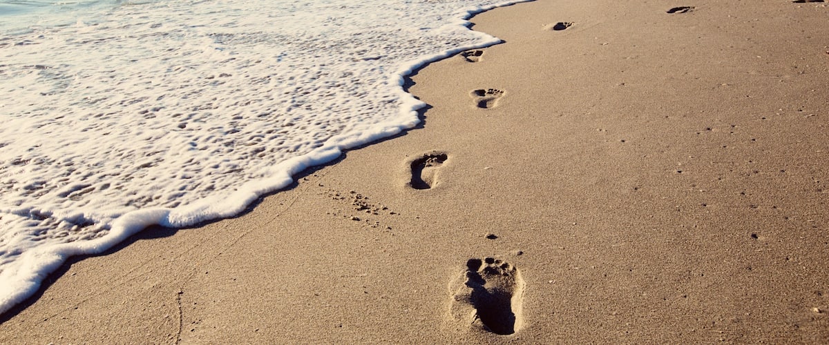 A sandy beach with footprints leading to the water.