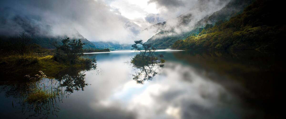 A serene lake surrounded by mountains, with a clear reflection of the sky and vegetation.