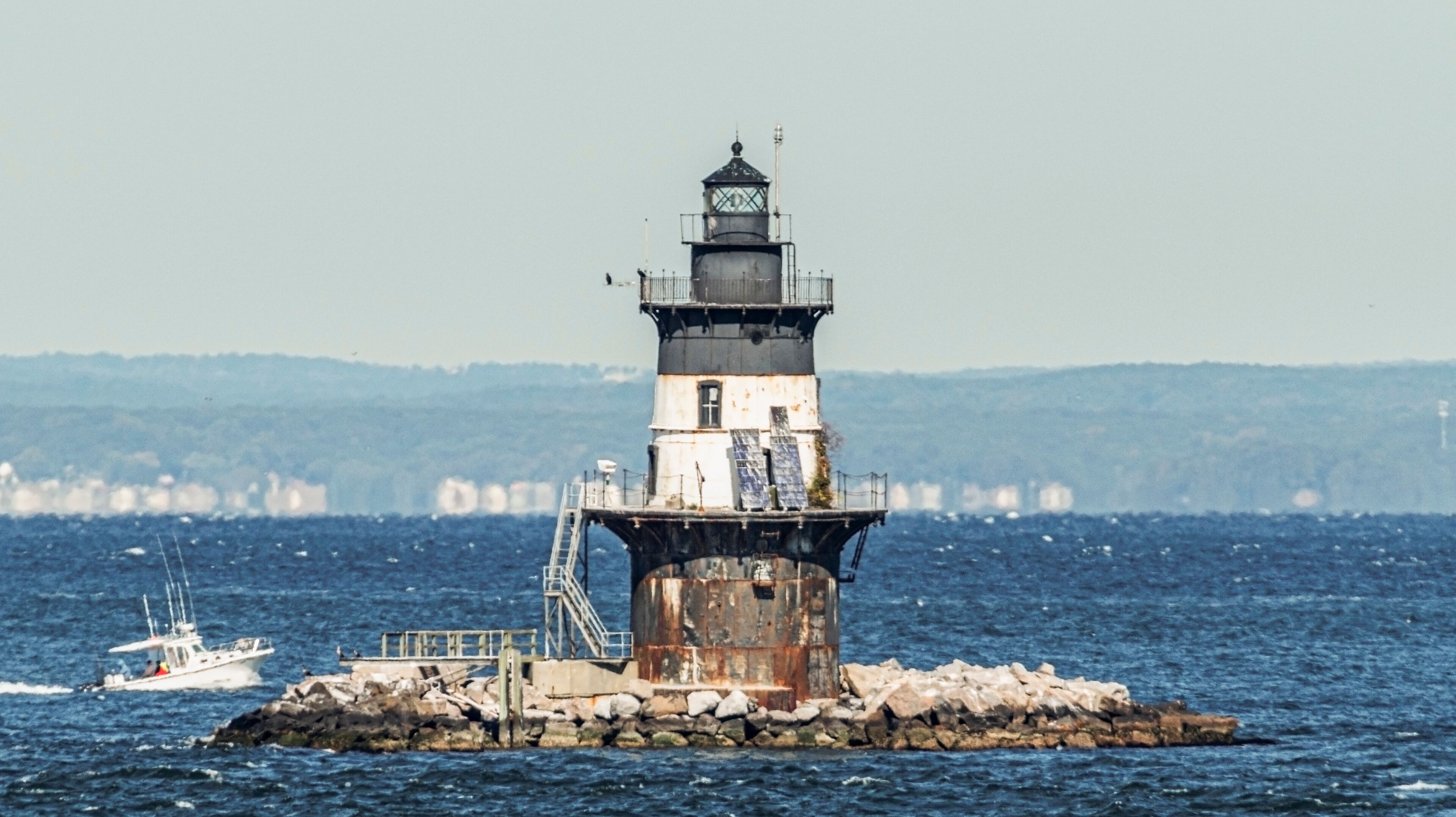 A lighthouse on a rocky outcrop with a boat in the water.