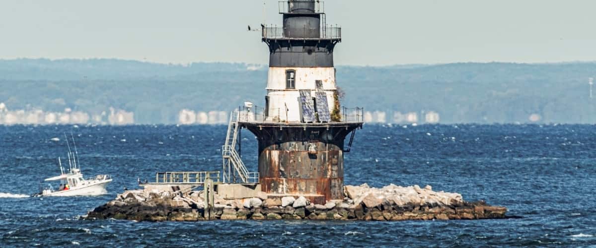 A lighthouse on a rocky outcrop with a boat in the water.