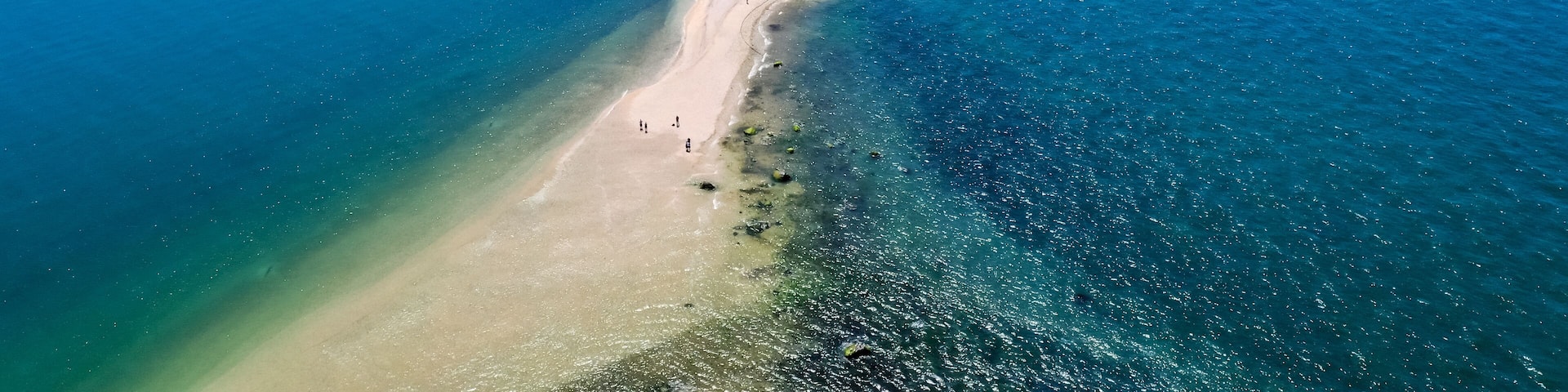 An aerial view of a coastal area with a sandy beach, a small settlement, and a clear blue sea.