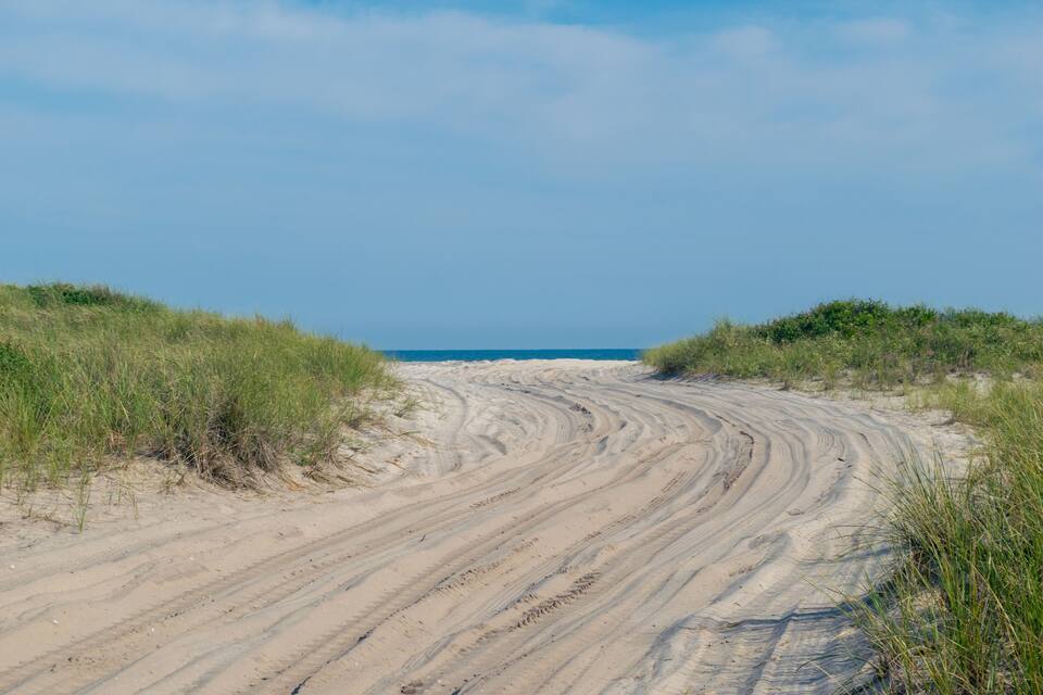 A sandy path leading to a beach with grassy dunes on either side.