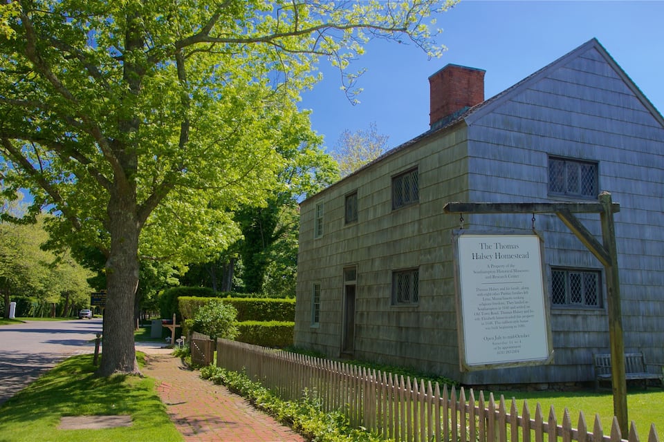A historical homestead with a wooden exterior, a brick chimney, and a signboard detailing its history.