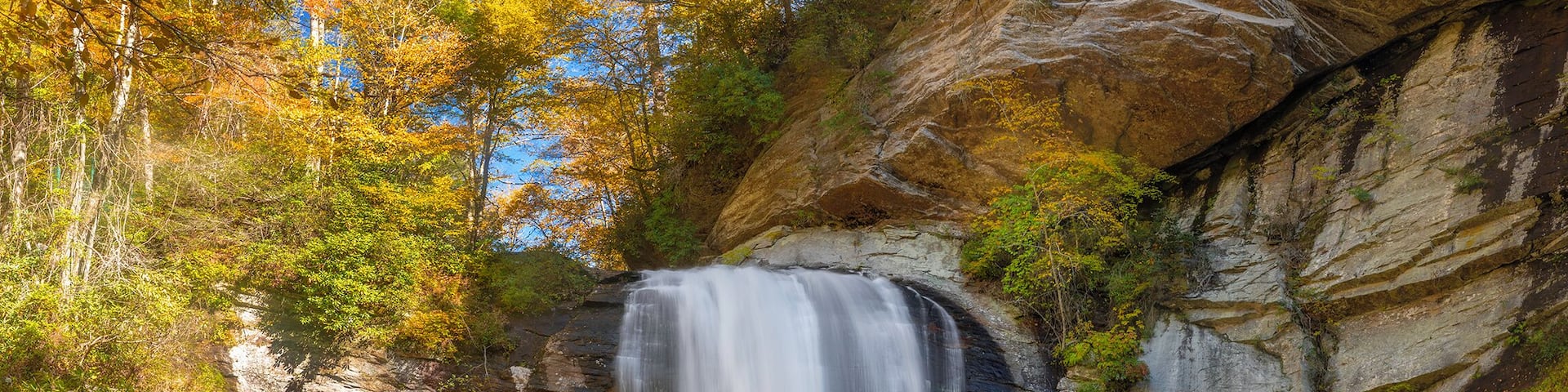 A waterfall cascading down a rocky cliff surrounded by autumn foliage.