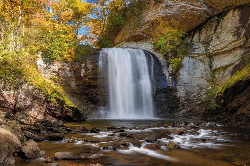 A waterfall cascading down a rocky cliff surrounded by autumn foliage.