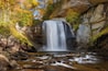 Una cascada se precipita por un acantilado rocoso rodeado de follaje otoñal.