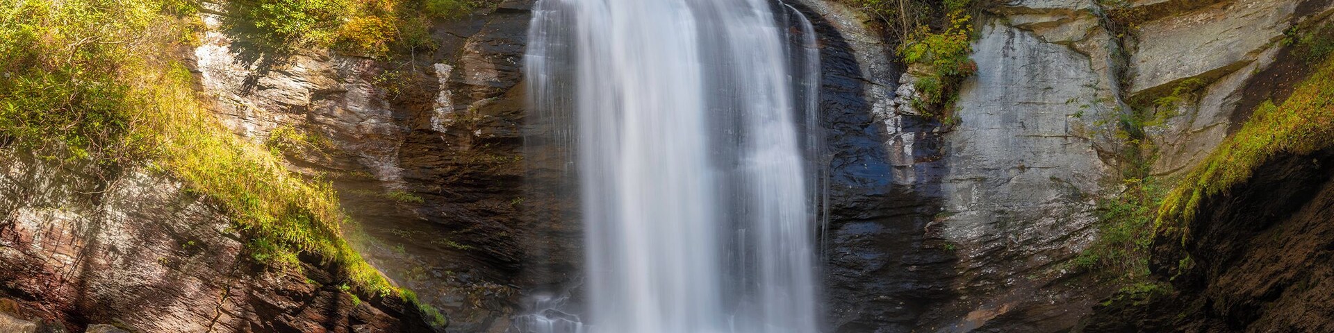 Uma cascata despenca por um penhasco rochoso, emoldurada por folhagem outonal.