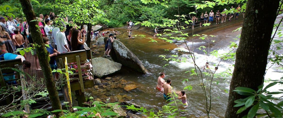 Sliding Rock which includes a river or creek and forests as well as a large group of people