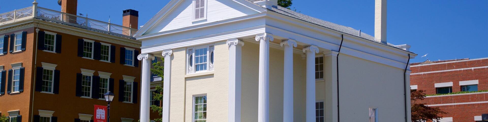 A classical building with white columns and a pediment, surrounded by other historic buildings.